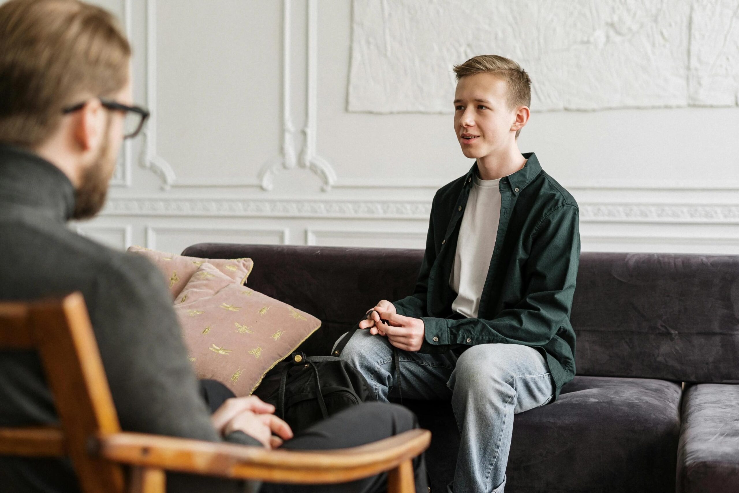 "A young man sits on a dark couch, attentively engaged in a career counseling session with a professional.